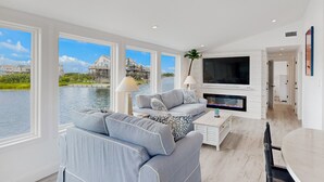 A spacious living room with a large window overlooking a body of water, a fireplace, and a modern TV.