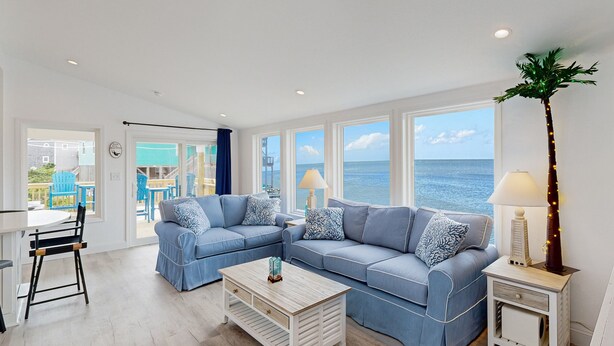 A spacious living room with a large blue sectional sofa, a wooden coffee table, and a view of the ocean through large windows.