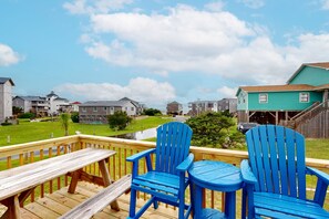 A wooden deck with two blue Adirondack chairs and a small table, overlooking a residential area with houses and a grassy field. - Waterfront, Dog-Friendly Home w/ Sound View, Private Hot Tub, Dock & Shared Pool (Avon)
