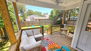 A covered outdoor patio with a wicker sofa, a small table, and blue chairs. - Salty Escape: Newly Constructed Retreat (Oak Island)