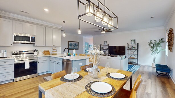 A modern kitchen with white cabinets, stainless steel appliances, and a wooden dining table set for four. - Salty Escape: Newly Constructed Retreat (Oak Island)