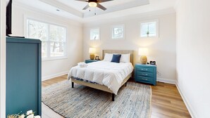 A bedroom with a bed, nightstands, a ceiling fan, and a window. - Salty Escape: Newly Constructed Retreat (Oak Island)