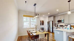 A modern kitchen with a wooden dining table, chairs, and a central island. - Salty Escape: Newly Constructed Retreat (Oak Island)