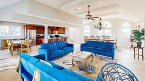 A spacious living room with blue sofas, a coffee table, and a chandelier. - Multi-level dog-friendly oceanfront home with private pool & hot tub, rec room (Salvo)