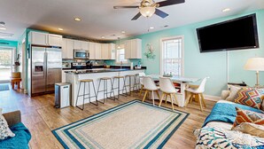 Una cocina moderna con una isla central, taburetes de bar y un área de comedor con un televisor montado en la pared.