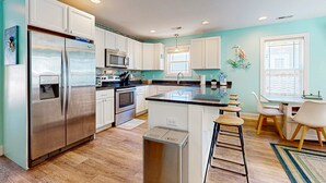 Una cocina moderna con armarios blancos, electrodomésticos de acero inoxidable y una isla central con taburetes de bar.