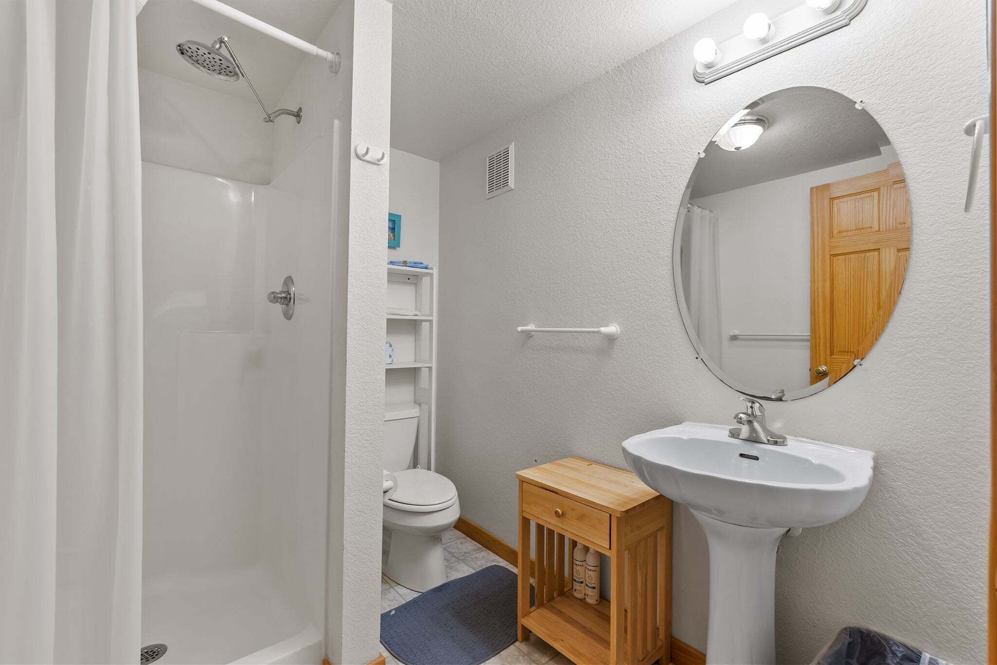 A bathroom with a shower, toilet, sink, and mirror.