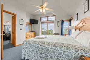 Quarto com cama, ventoinha no teto, cômoda, televisão e janela com cortinas.