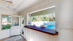 A covered porch with a wooden bench, a door, and a view of a backyard swimming pool.