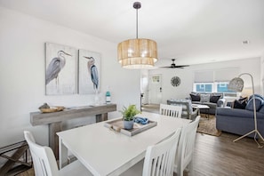 A modern living space with a dining area, a sofa, a coffee table, and a large window.