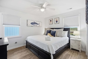 A bedroom with a bed, a nightstand, a ceiling fan, and a window with blinds.