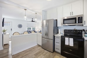A modern kitchen with white cabinets, stainless steel appliances, and a wooden floor.