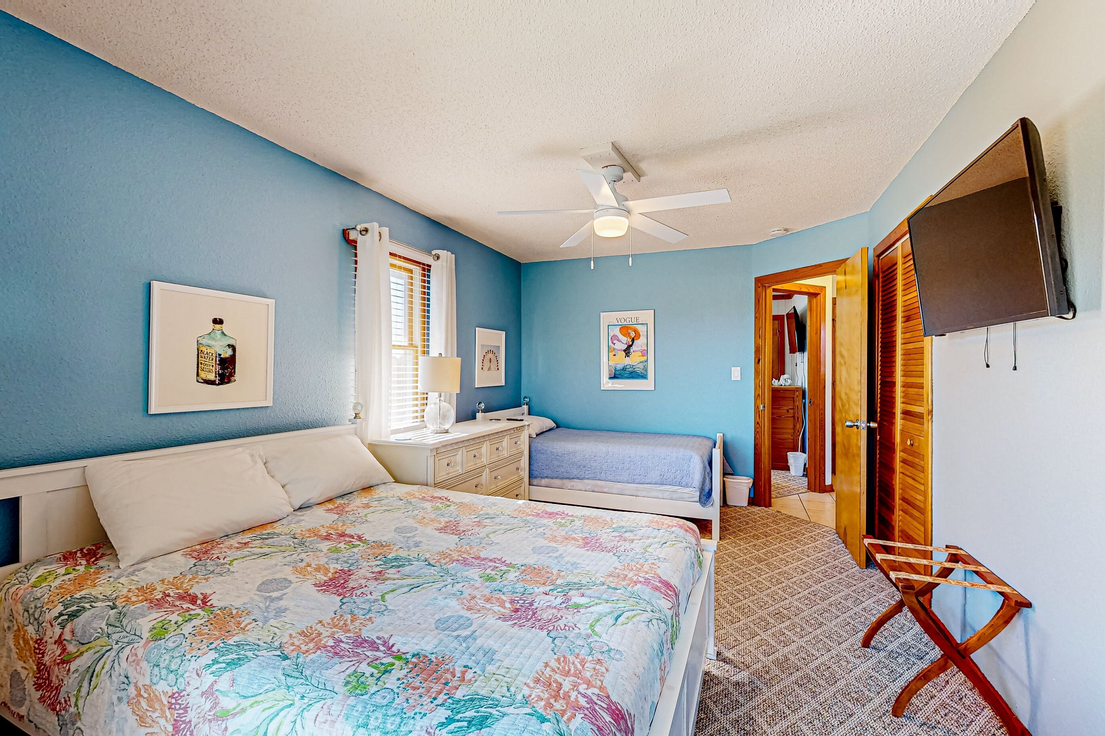 Une chambre à coucher comprenant un lit, une commode, un ventilateur de plafond et un téléviseur.