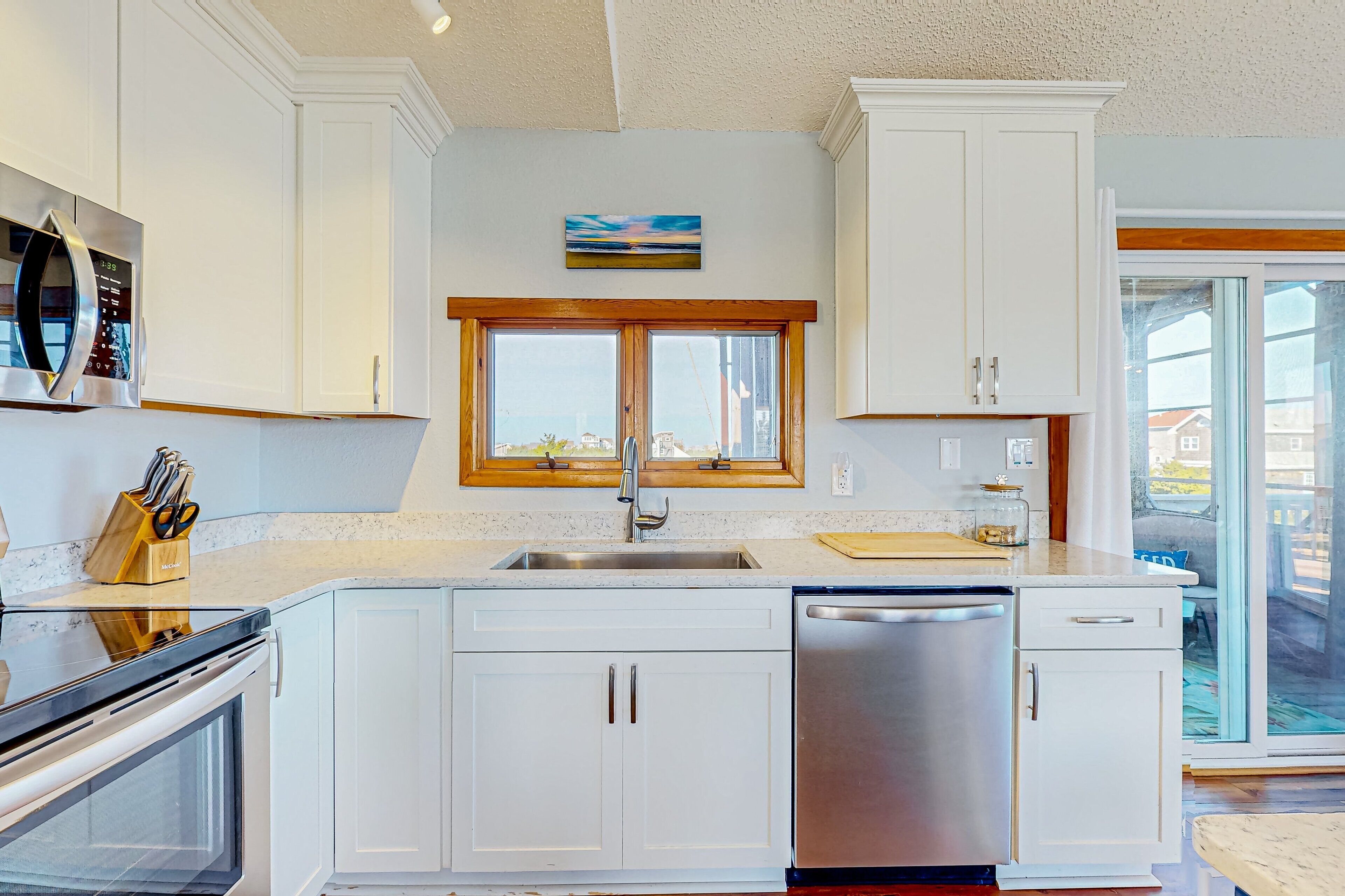 A modern kitchen with white cabinetry, a stainless steel dishwasher, and a window with a view of the outside.