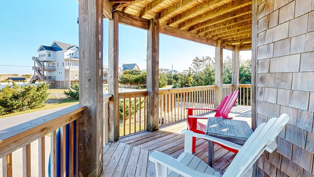 Una terraza de madera con una mesa y sillas, con vistas a una playa y casas.