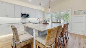 Una cocina amplia con armarios blancos, una isla grande con taburetes de bar e iluminación colgante.