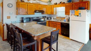 Una cocina con armarios de madera, encimera de granito, refrigerador, microondas y pileta.