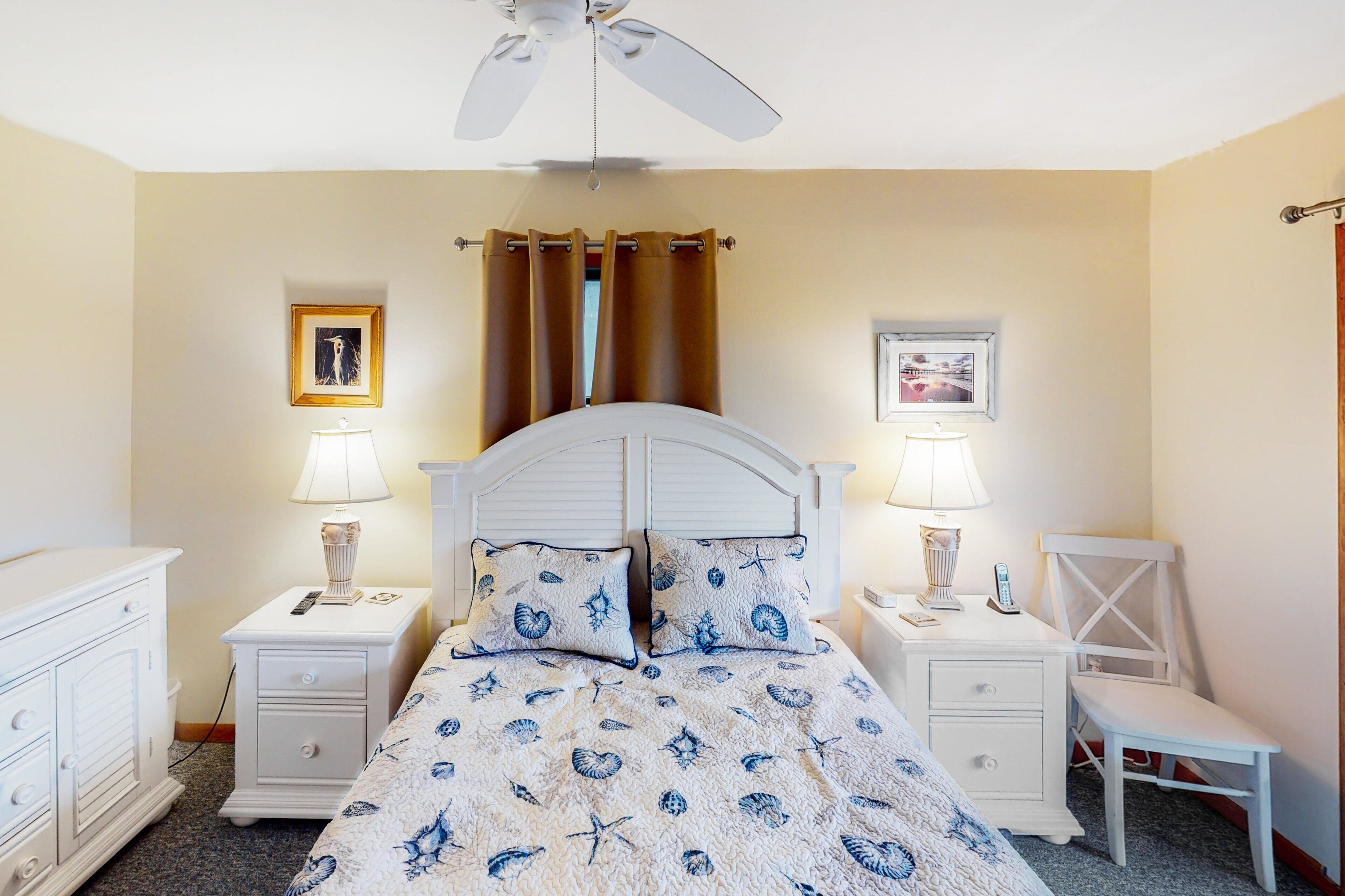 A bedroom with a bed, two bedside tables, a chair, a ceiling fan, and two wall-mounted lamps.