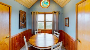 Un comedor con una mesa y sillas de madera, una ventana con cortinas y un techo de madera.