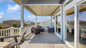 A covered deck with outdoor furniture, a railing, and large windows. - The Doobler: Ocean Views, Near Beach and Golf (Ocean Isle Beach)