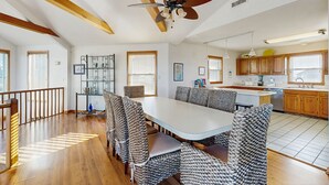 Un comedor amplio con una mesa larga y sillas estampadas, un ventilador de techo y vigas de madera.