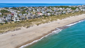 Vista aérea de una zona residencial costera con propiedades frente a la playa, una playa de arena y una vista despejada del océano.