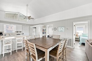 Una cocina amplia con una isla central, muebles blancos y un comedor con mesa y sillas de madera.