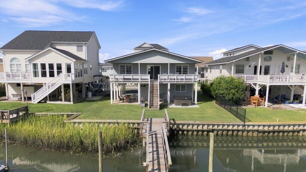 A waterfront property with a dock leading to a house with a covered porch and a second-story balcony.