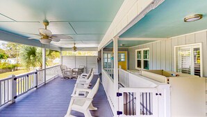 A covered porch with white railings, a ceiling fan, and a row of white plastic chairs.
