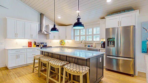 A modern kitchen with white cabinets, a stainless steel refrigerator, and wooden bar stools.