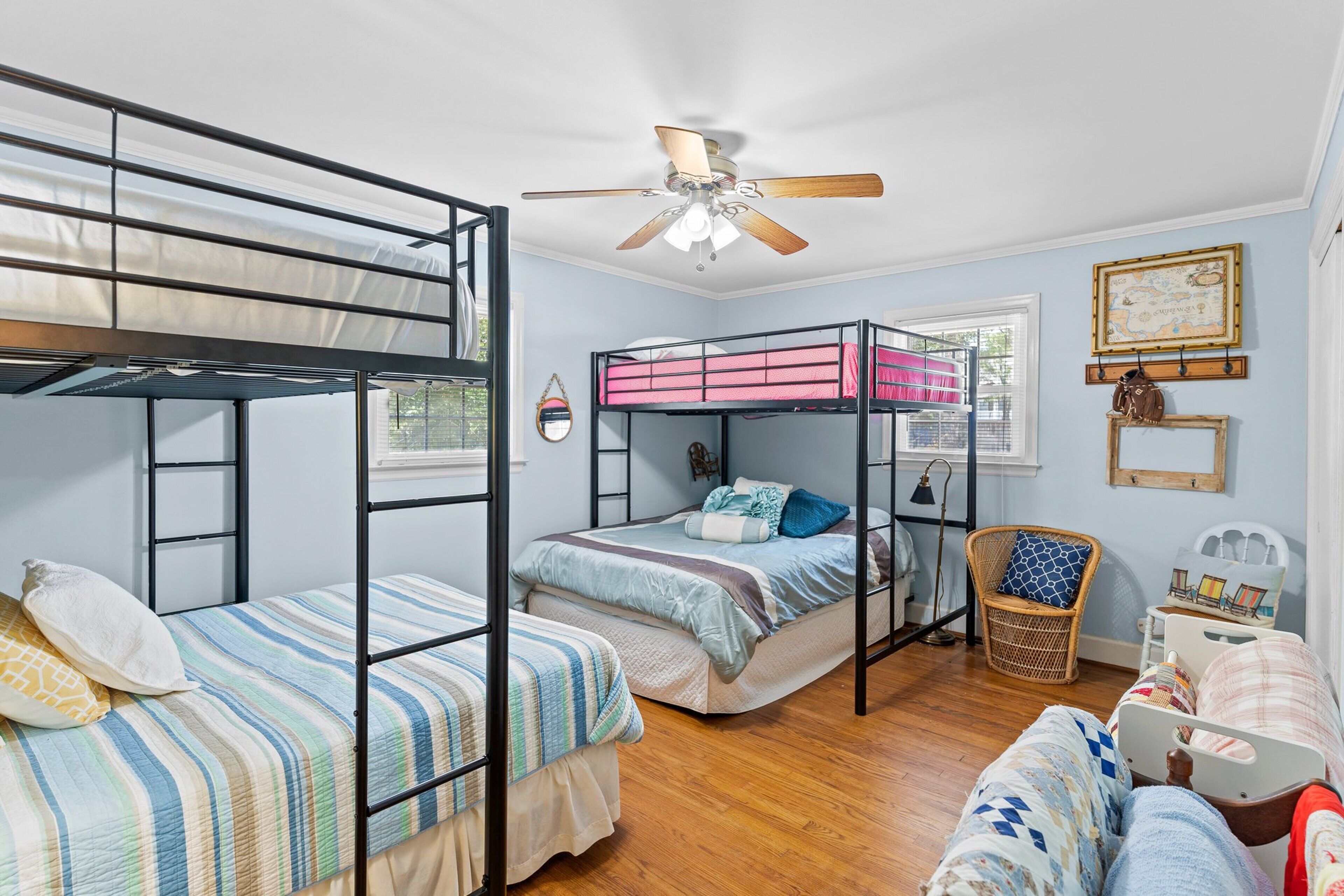 A room with bunk beds, a ceiling fan, a wicker chair, and a small table with a lamp.