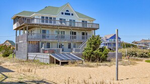 Et flere-etagers hus ved stranden med balkon, solpaneler og en sandstrand i forgrunden.