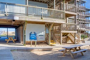 Une maison de plage en bois avec une terrasse, un panneau indiquant « Batter’s High », et une table de pique-nique.