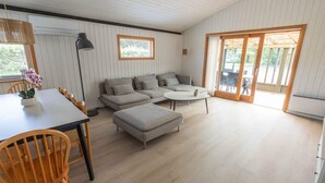 A modern living room with a sofa, ottoman, and round coffee table. There is a dining table with chairs and a potted plant. - 4 Star Holiday Home in Vaeggerlose (Vaeggerlose)