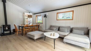 A cozy living room with a sofa, ottoman, dining table, chairs, a fireplace, and a window with blinds. - 4 Star Holiday Home in Vaeggerlose (Vaeggerlose)
