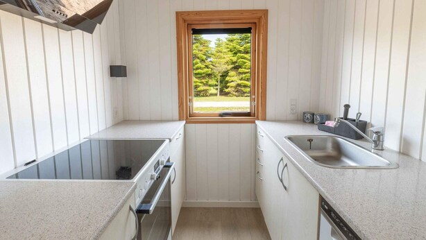 A compact kitchen with white cabinetry, a built-in oven, a double sink, and a window with a view of greenery. - 4 Star Holiday Home in Vaeggerlose (Vaeggerlose)