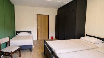 Een kamer met twee éénpersoonsbedden, een houten garderobe, een stoel en een deur.