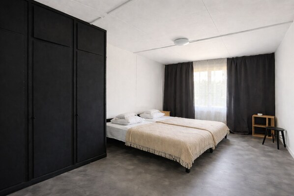 A minimalist bedroom with a bed, a wardrobe, a small stool, and a window with curtains.