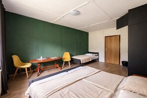 A room with two beds, a small table with chairs, a wooden door, and a green wall. - Carlsbad Wellness & Camping Resort (Březová)