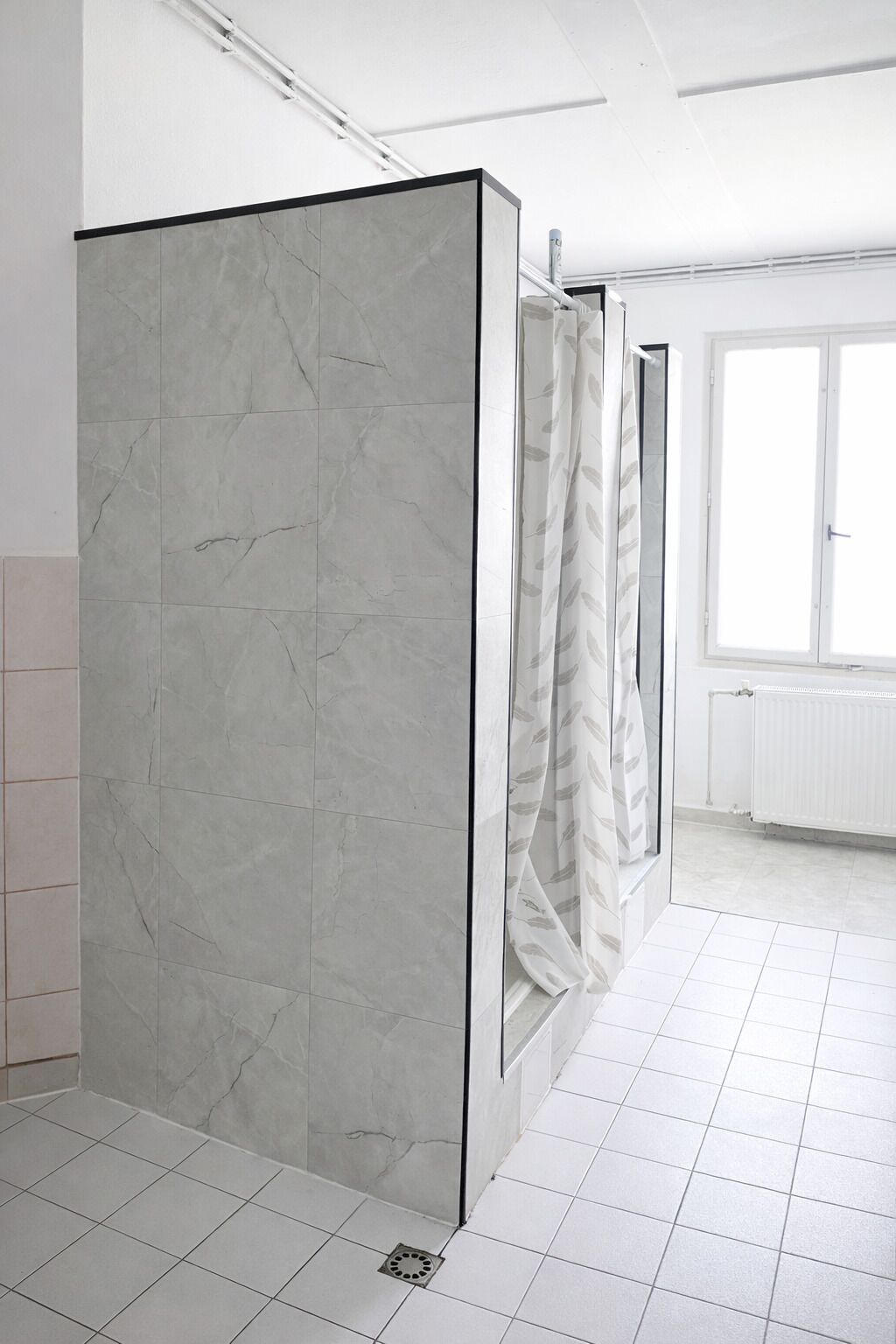 Un baño con separador de mármol, cortina de ducha y ventana con vistas.