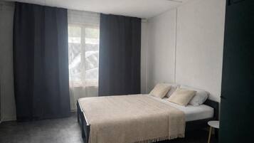 Un dormitorio con cama, una mesita y una ventana con cortinas.