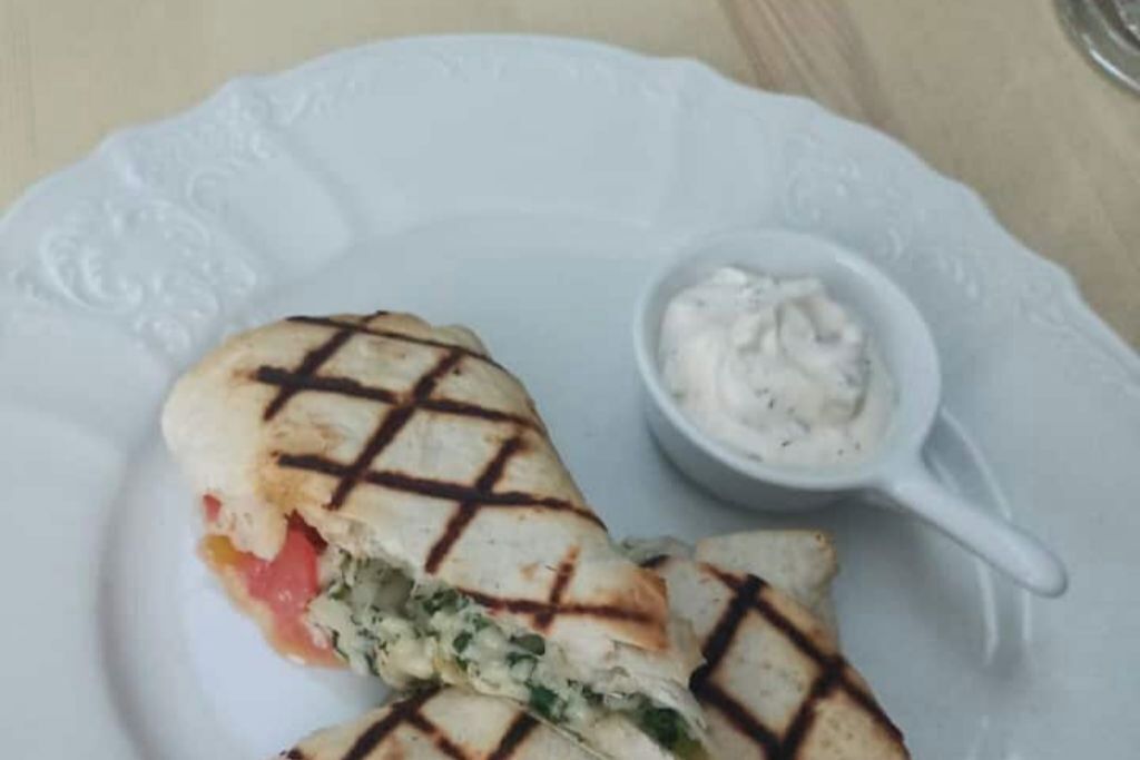 A plate with a grilled sandwich and a small bowl of sauce.