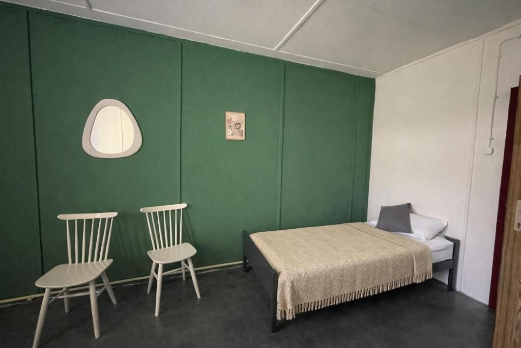 Een kamer met een bed, twee stoelen, een tafeltje, een spiegel en een foto aan de muur.