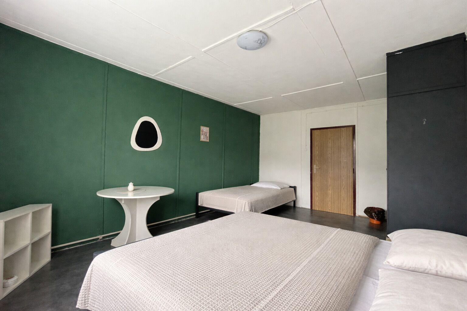 Una habitación con una cama, una mesita pequeña, un espejo en la pared y una puerta.