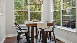 Un coin repas avec une table en bois et quatre chaises, de grandes fenêtres donnant sur un paysage verdoyant et un lustre.