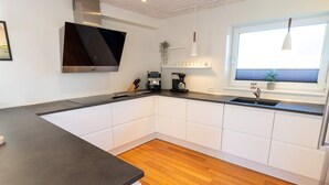 Une cuisine moderne avec des meubles blancs, un plan de travail foncé, une cuisinière encastrée et une fenêtre équipée de stores.