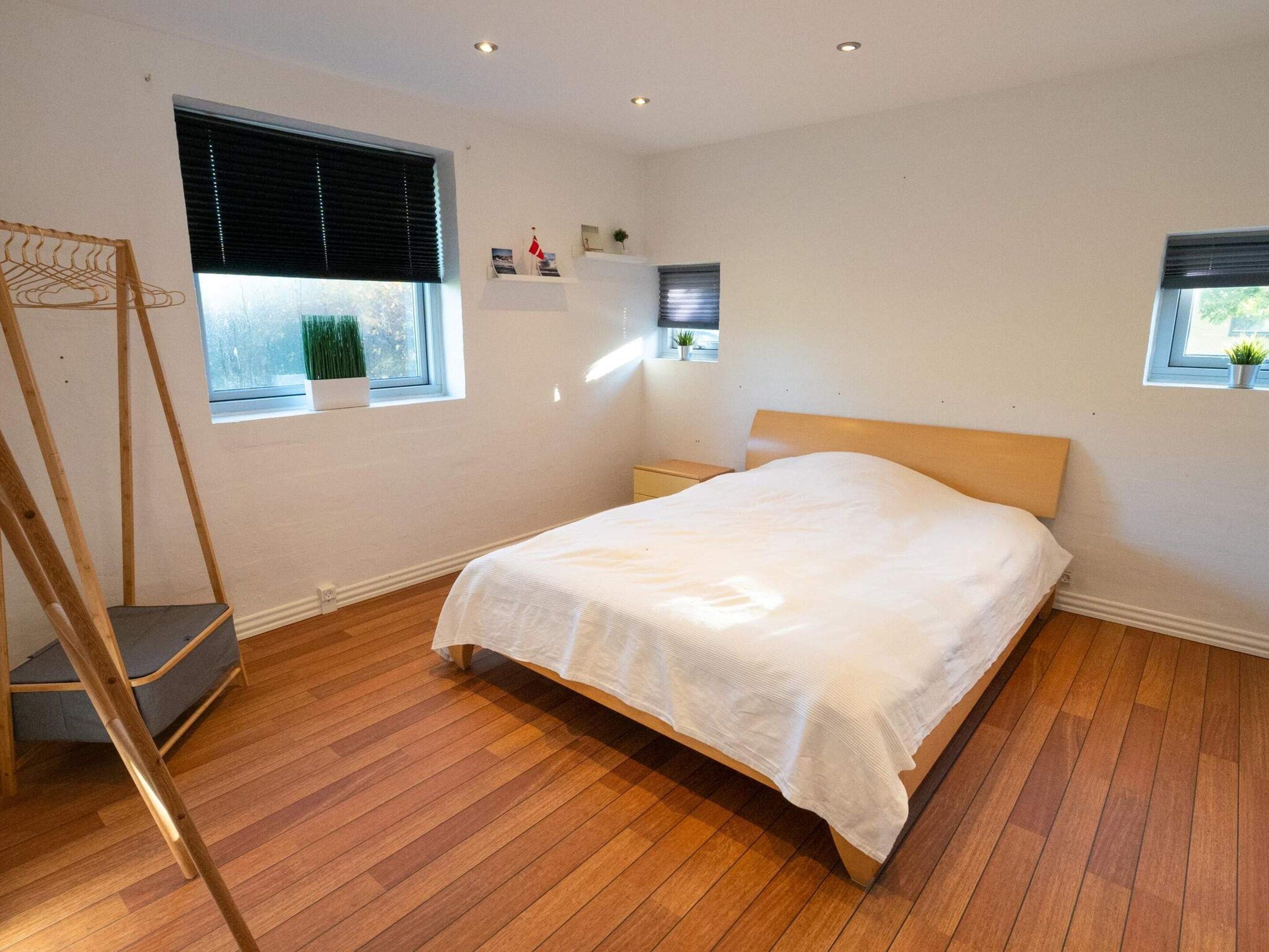 Ein Schlafzimmer mit Holzboden, einem Bett mit weißer Bettwäsche, einer Holzleiter und zwei Fenstern mit Jalousien.