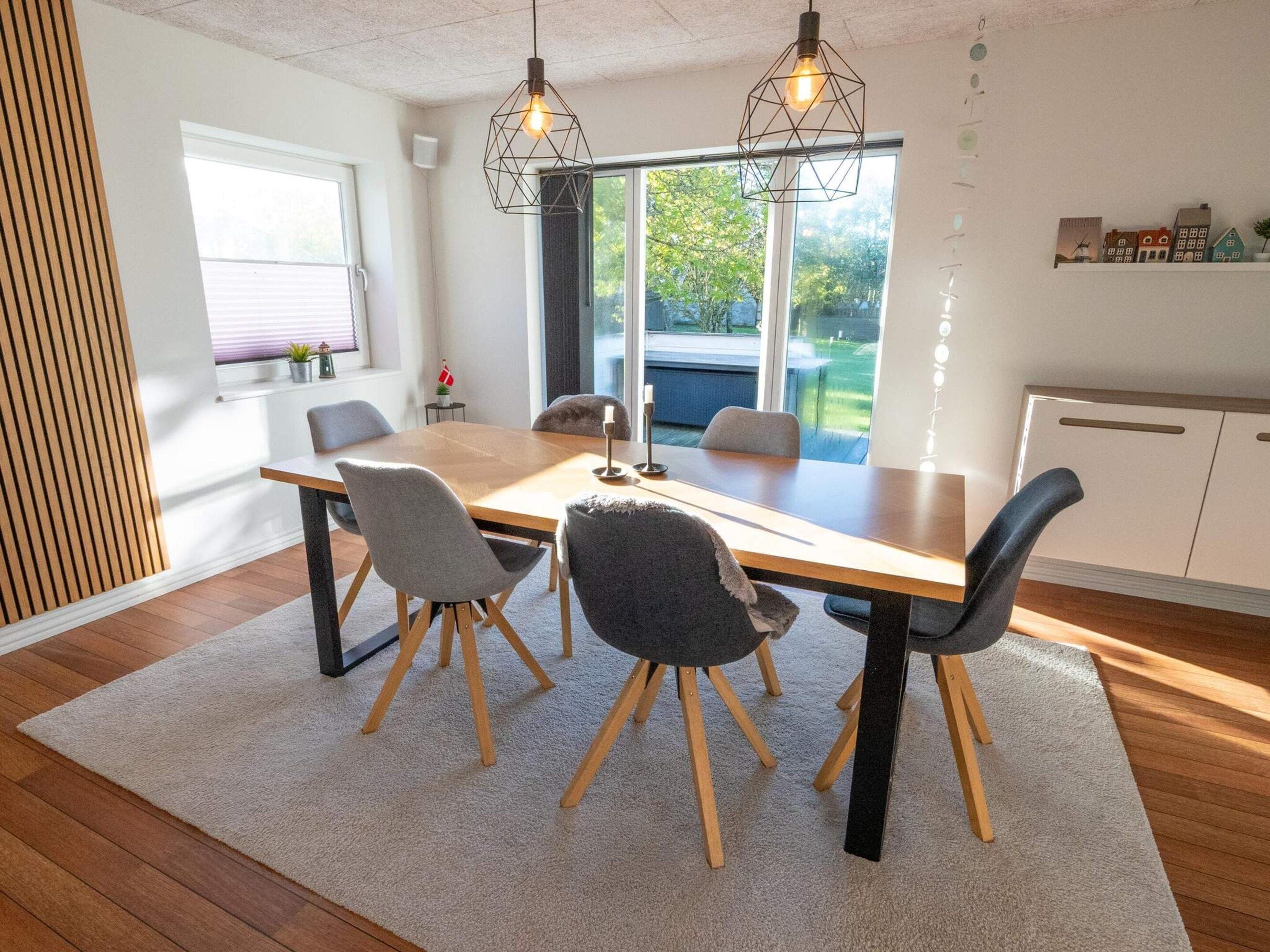 A modern dining area with a wooden table, four chairs, and pendant lighting.