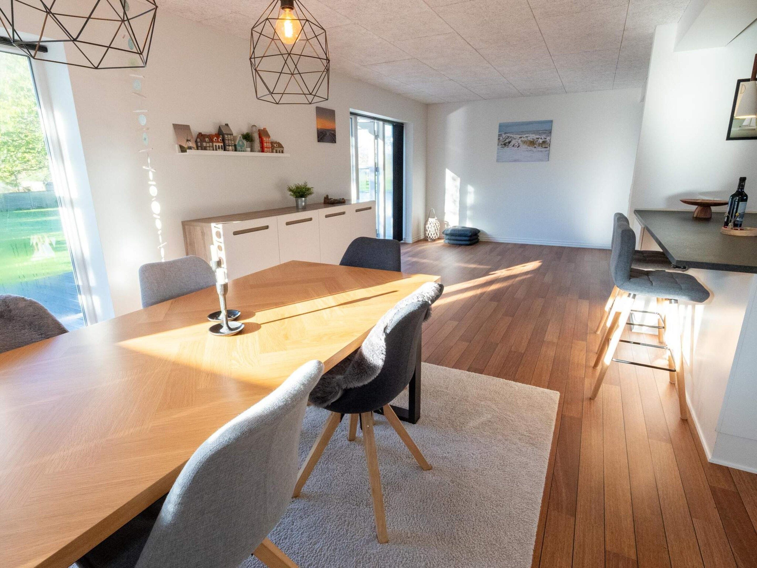 A modern dining area with a wooden table, grey upholstered chairs, and a geometric pendant light.