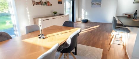 Un espace repas moderne avec une table en bois, des chaises à revêtement gris et un luminaire suspendu aux motifs géométriques.
